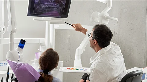 A dentist is explaining some radiographic findings to a patient in a dental chair.