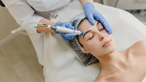 A woman getting some cosmetic treatment using a handheld instrument by another person.