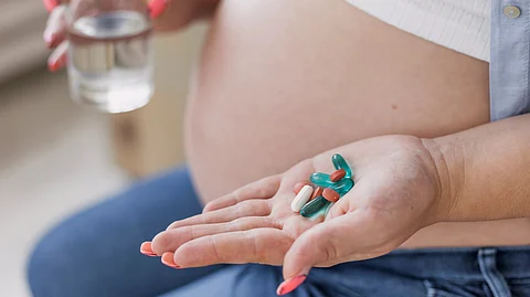 Image showing a pregnant woman with drugs in one hand and water in another.