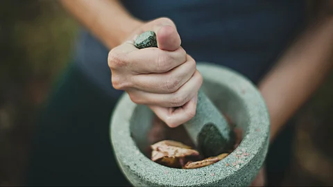A grey color mortar and pestle in a girl's hands having an ayurvedic herb.