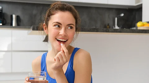 A brunette-haired woman taking a supplement with some water.