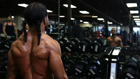 An image from behind shows a man working out whose reflection is visible in the mirror ahead.