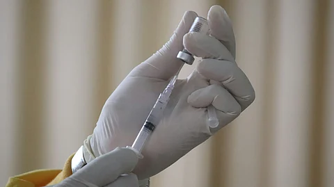 A close-up image of a syringe drawing vaccine from a glass ampule, with clear liquid inside and a gloved hand holding the ampule steadily.