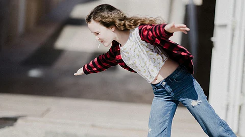 A girl wearing a red checkered shirt with white printed top and a jeans slightly tilted forward for a pose.
