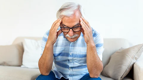 Image shows elderly man holding his head in stress.