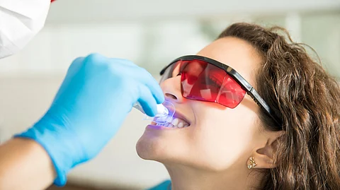 Image shows dentist fitting a mouthpiece for patient wearing protective glasses.