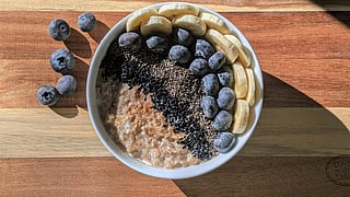 Healthy breakfast bowl with oatmeal topped with sliced bananas, blueberries, chia seeds, and black sesame seeds, placed on a wooden table with extra blueberries on the side.