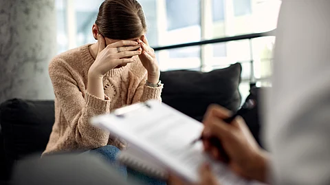 Depressed woman wearing a brown sweater and getting counselling from a doctor.