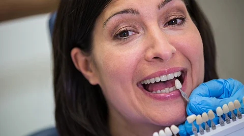 Dentist examining female patient with teeth shades.