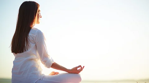 Image shows woman doing meditation in sunlight.