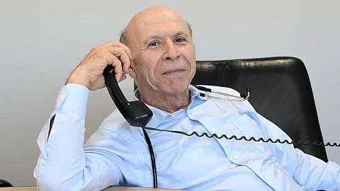 An old man speaking to someone on a telephone wearing a blue shirt and a stethoscope.