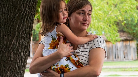 A woman holds a young girl in her arms outdoors.