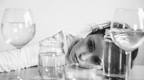 A black and white image depicts a girl looking at glasses of alcohol.
