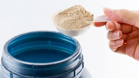 A scoop of meal replacement shake powder taken from a blue container against a white background.