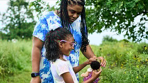 Mother and daughter holding flowers and a doll together outside in the park.