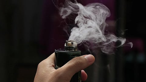 A person holding a black vape in his hand.