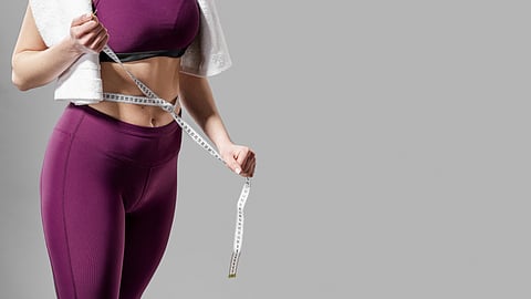 Woman in fitness wear measuring waist with tape after workout, symbolizing weight loss and body transformation.