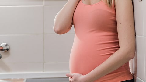 Image of a pregnant woman wearing pink top standing in a bathroom.
