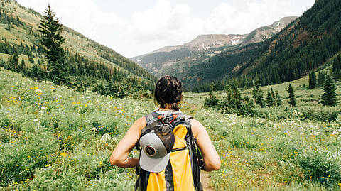 Image of a woman hiker carrying an orange backpack on mountain.