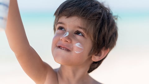 Image of a young boy looking up while having sun protection cream applied to his face.