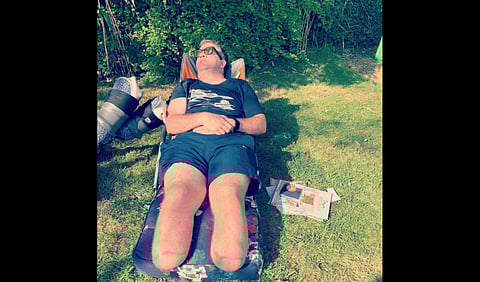 An image of Neil Hopper lying on a mat on grass soaking up sunshine.