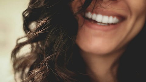 Close-up image of a woman having curly hairs smiling and showing her teeth.