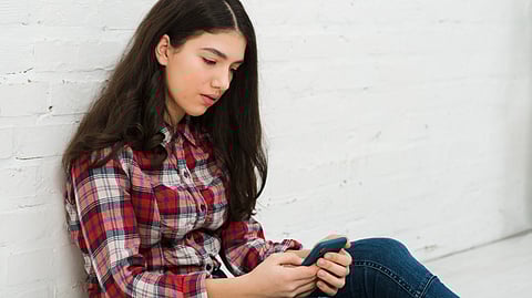 A teenage girl sitting alone and browsing in phone.