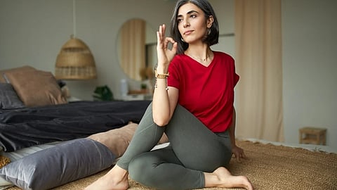 Portrait of gray haired cute young female in casual clothes sitting on floor doing ardha matsyendrasana or sitting half spinal twist, practicing yoga, stimulating digestive system in the morning.