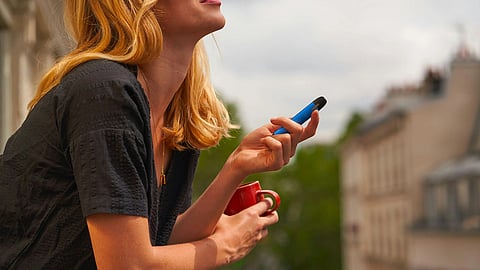 A woman holding a blue colored vape and a red cup standing in the balcony.