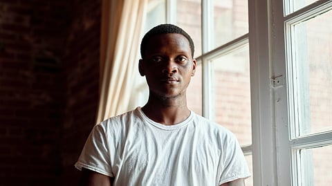 Image of a person wearing a white t-shirt standing besides a window.