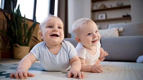 Image of two babies crawling over the floor and smiling.
