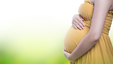 Image of a pregnant woman wearing a yellow dress in front of a blurry background.