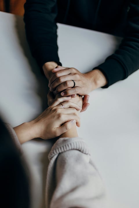 Two people holding hands on a table, symbolizing connection and mental support