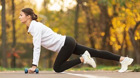 Image of a woman exercising in black trackpants and white jacket.