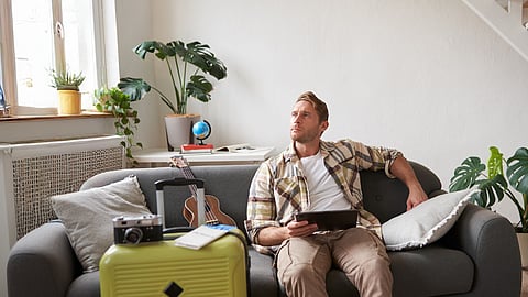 Image of a man wearing a white t-shirt and checkered shirt sitting on a sofa in his living room.