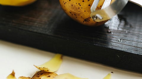 Image of a potato and it's peels on a chopping board.