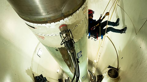 Worker installing a green cylindrical rocket or missile with a metallic top.