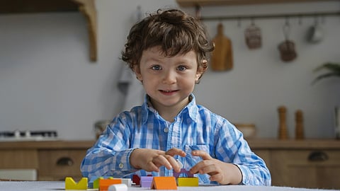 Image of a child wearing blue checkered shirt playing with blocks in a household setting.