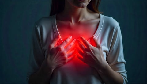 A woman clutching her chest in pain, with a glowing red area over her chest symbolizing heart pain or discomfort.