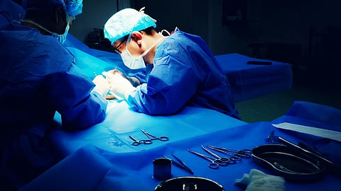 Two surgeons perform a procedure on a patient in a sterile operating room, focused on their tasks.
