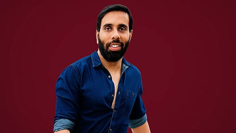 An image of Dr. Anshul Gandhi in a blue shirt in maroon background.