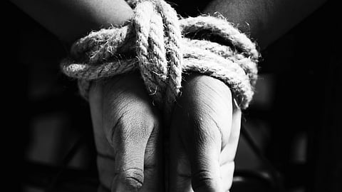 Black and white image of hands tied with ropes.