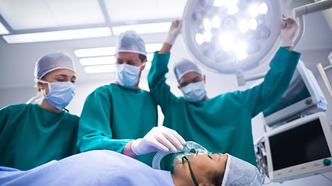 Surgeons adjusting lighting and oxygen mask on patient mouth in operation theater.
