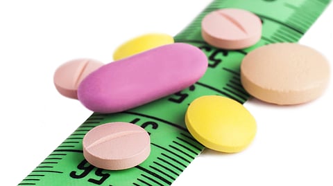 A measuring tape and few colored tablets spread over tghe tape.