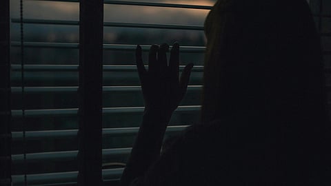 Image of a woman looking out of the window in a dark night.