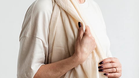 Close-up image of a woman’s hands holding a white scarf while she wears a white T-shirt.