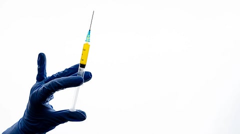 Image of a hand wearing surgical gloves and holding an injection.