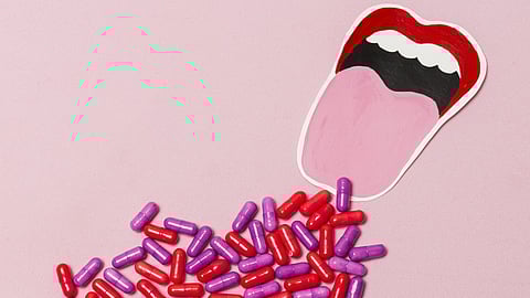 An image of an open mouth with a pink tongue on a pink background,with red and purple capsules.