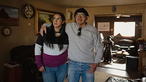 An image of elderly man and young woman stand side by side in a cozy, warmly lit living room.