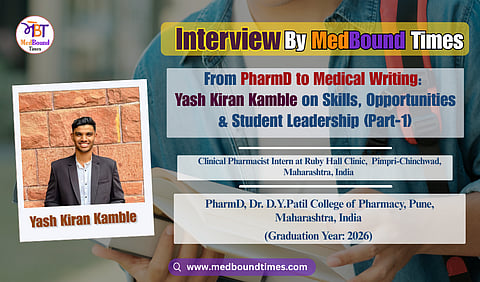 Smiling man in a black suit jacket and white shirt stands against a textured red brick wall. The image conveys a confident, cheerful tone.